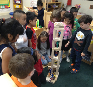 Two children describe their apartment tower to the rest of the class. We often share photos like this  with families to illustrate their child’s work and creativity. The photo also  demonstrates how valuable it is for children to explain and take pride in their  work.