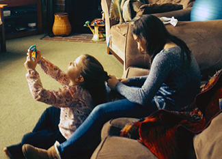 Older sister braiding younger sister's hair while younger is playing on a smartphone