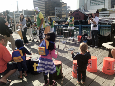 On a terrace, children participate in a drumming circle with Grooversity.